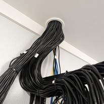 Dark network cables passing through a round white port at the ceiling