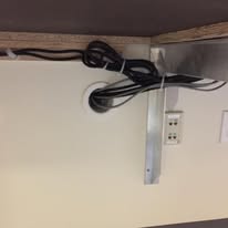 Cables passing through a round port under a desk near an outlet