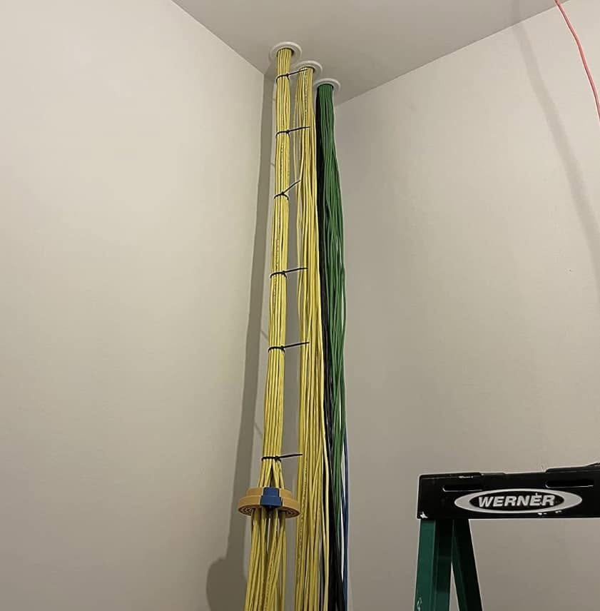 Yellow, green and dark network cable bundles entering separate round ports near an IT room ceiling